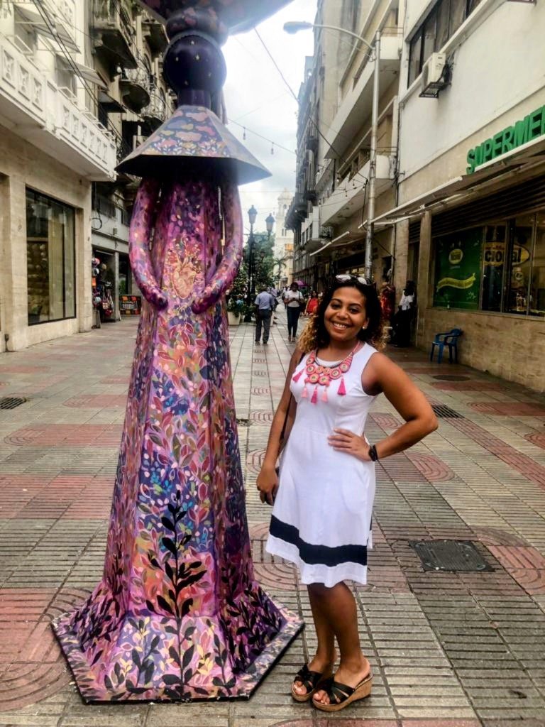 a woman stands next to a colorful statue