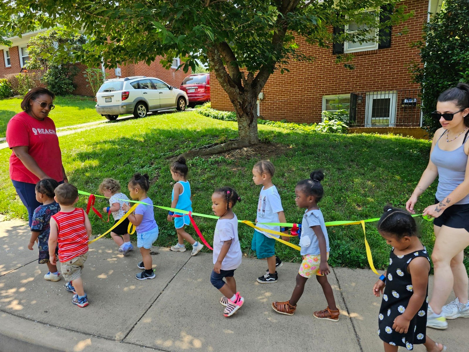 children walk along a sidewalk aided by caretakers